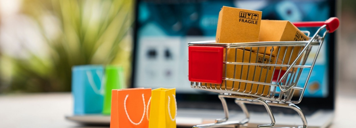 Pakketten in een winkelwagen met wat boodschappentassen met op de achtergrond een laptop en een webshop voor online winkelen