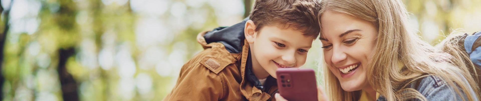 Gelukkige moeder en zoon wandelen in het bos. Ze gebruiken kaarten op smartphones.